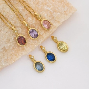 Close-up of oval gemstone pendant necklaces in multiple colors with matte gold finish