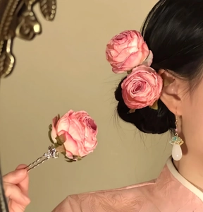 Close-up showing a pink rose flower hair fork worn on hair buns and held in hand