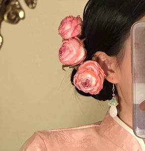 Close-up detail of elegant pink rose hair pins and teardrop earring worn by a model