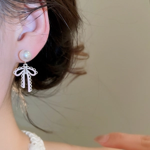 Close-up detail of a silver needle pearl earring featuring a delicate pink bow design.