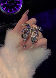 Detail view of a large silver textured butterfly open ring on a hand with luxury nails.