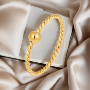 Dettaglio macro di un elegante anello a treccia in acciaio titanio dorato con perla.