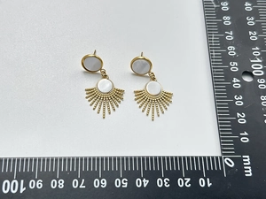 Detail view of gold sunburst earrings with natural shell inlay beside a measurement ruler