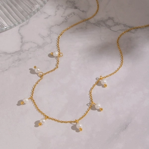 Detail of minimalist 18K gold plated pearl necklace on a marble background