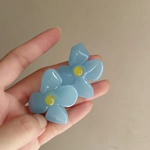 Close-up view of elegant blue acrylic flower earrings held in hand for detail display
