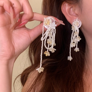 Detailed close-up of handmade white beaded tassel earrings with sweet flower charms