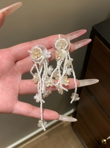 Detailed view of white beaded flower tassel earrings with translucent petals held in hand.