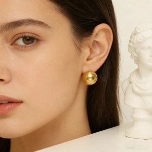 Minimalist golden polished sphere stud earrings shown on model with artistic statue