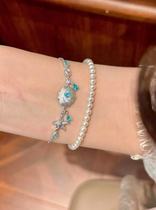 Detaillierte Makroansicht von Silberarmband mit Muschel und Seestern neben weißen Perlen
