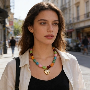 Dettaglio di una collana di perle in resina colorata con un grande ciondolo a cuore in oro lucido.
