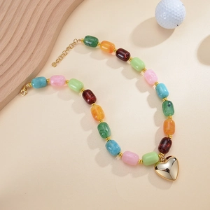 Dettaglio di una collana di perle in resina colorata con ciondolo a cuore dorato lucido.