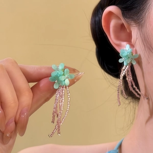 Detailed view of pink beaded tassel earrings with light green flowers on ear and hand.