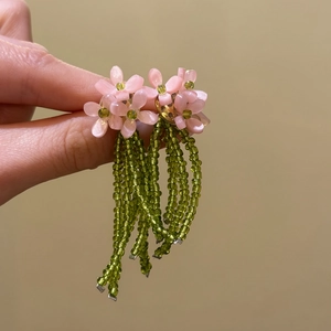 Close-up detail of fresh pink flower stud earrings with long green beaded tassels