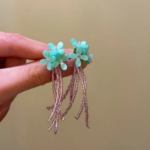Detail shot of light blue flower stud earrings with elegant pink beaded tassels