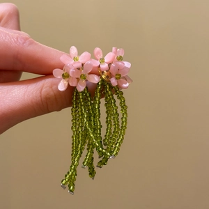 Detailed view of hand holding pink beaded flower earrings with long green tassels