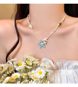 Close-up detail of a blue and white starfish pendant necklace with pearls on a model
