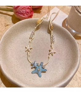 Close-up of a handmade ocean-themed necklace with blue starfish and white shells beads.