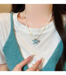 Close-up of blue starfish necklace with pearls on white cord worn by a woman.