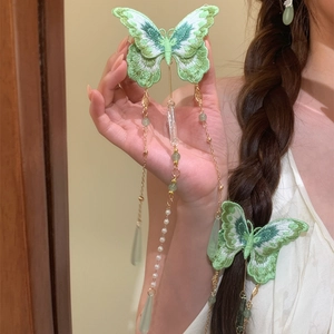 Detailed view of green knitted butterfly hair clip with pearl and teardrop tassels.