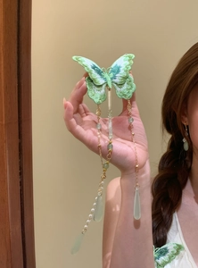 Detailed view of an embroidered green butterfly hair clip with long pearl tassels