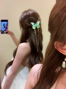 Detailed view of a green knitted butterfly hair clip with elegant pearl tassels in hair.