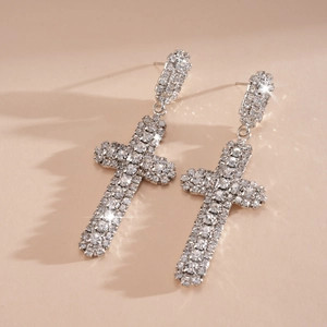 Détail de boucles d'oreilles en forme de croix argentée avec pavé de strass étincelants.