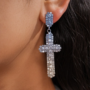 Vue macro d'une boucle d'oreille en forme de croix sertie de strass bleu clair étincelants