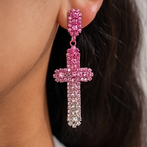 Gros plan de boucles d'oreilles croix élégantes en strass dégradé rose portées par un mannequin