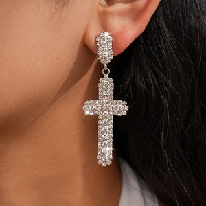 Détail de boucles d'oreilles pendantes en forme de croix serties de strass brillants.