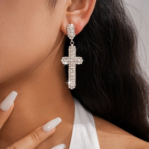 Boucles d'oreilles croix argentées avec strass complets portées par un modèle