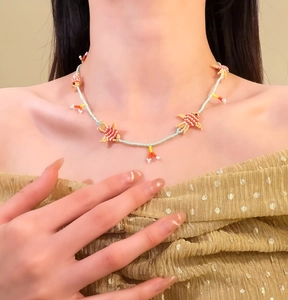 Dettaglio di una collana di perline fatta a mano con ciondolo a pesce indossata qui