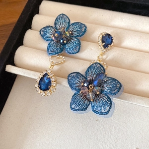 Detailed view of asymmetric blue embroidered flower earrings with teardrop crystals