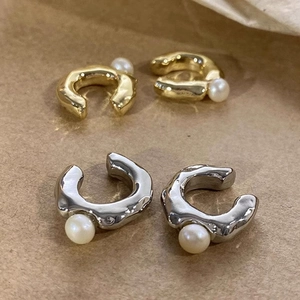 Close-up of elegant gold and silver pearl ear cuffs with organic wavy metal design.