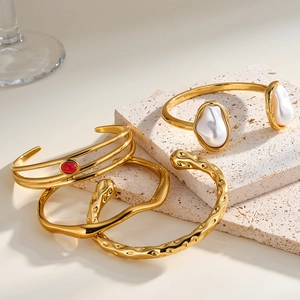 Dettaglio di bracciali a cerchio in acciaio inox dorato con perle barocche e pietra rossa