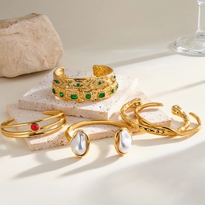 Dettaglio di lussuosi bracciali in acciaio dorato con accenti in smeraldo e perle eleganti