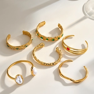Varietà di eleganti bracciali rigidi in acciaio dorato con smeraldi e perle.