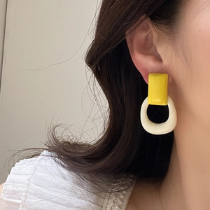 Primer plano de pendientes geométricos retro en resina amarilla y crema en una modelo