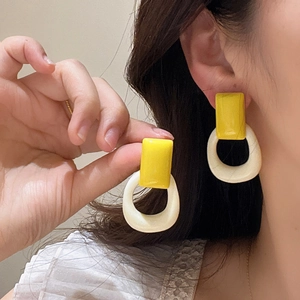 Detalle de pendientes geométricos de resina amarilla y crema puestos