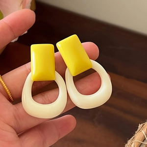 Primer plano de pendientes retro de resina geométrica en amarillo vivo y blanco crema
