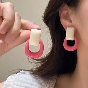 Primer plano de pendientes retro de resina en rosa y crema puestos en la oreja.