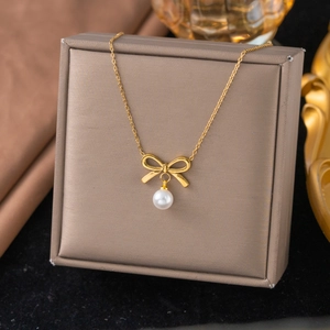 Elegante gouden strik ketting met ronde witte parel hanger op een juwelendoosje