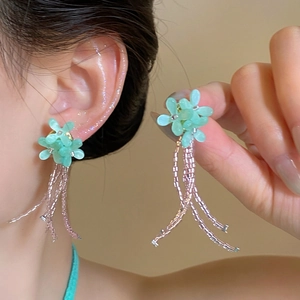 Gros plan de boucles d'oreilles fleurs vertes avec glands en perles pour look boho.
