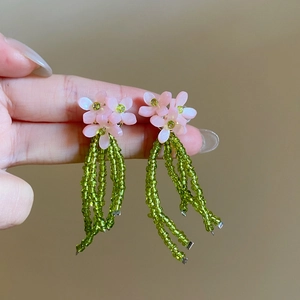 Détail macro de boucles d'oreilles fleurs roses faites main avec franges vertes.