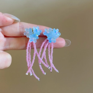 Détail de boucles d'oreilles fleurs bleues avec pompons en perles roses de vacances