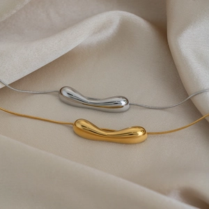 Close-up of minimalist 18K gold and silver streamlined pendants on snake chains