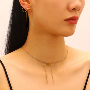 Macro detail of gold-plated stainless steel bow necklace and tassel earrings on model