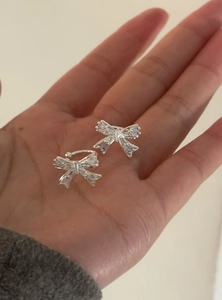 Gros plan de boucles d'oreilles nœuds argentées avec zircons brillants en main