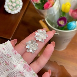 Detail of silver camellia flower stud earrings with sparkling crystals held by a hand.