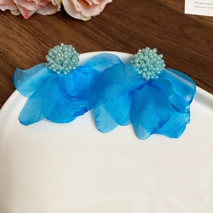 Close-up of vintage blue fabric flower earrings with bead details on a white plate