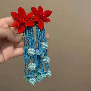 Detail view of vibrant red acrylic flower earrings with long blue beaded tassels